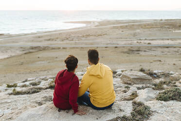 Father and son looking at view while sitting on rock - MIMFF00631