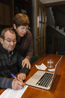 Älterer Mann mit Sozialarbeiter, der zu Hause am Laptop in einem Buch schreibt - XLGF01332
