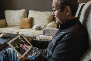 Smiling senior man on video call with his grandchildren through digital tablet at home during COVID-19 - XLGF01339