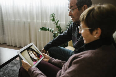 Grandparents on video call with granddaughter through digital tablet at home - XLGF01342