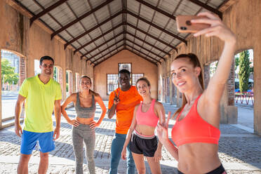 Eine Gruppe verschiedener Läufer in Sportkleidung steht auf der Straße und macht ein Selfie mit dem Smartphone während des Trainings im Sommer - ADSF21634