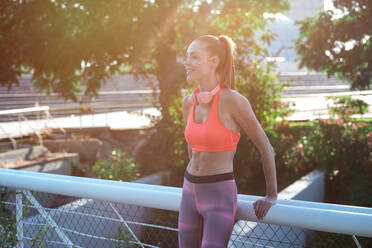 Confident fit female runner standing on street in summer and having break during training in city while looking away - ADSF21636