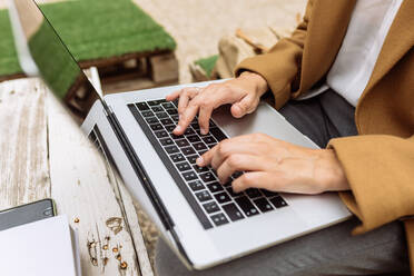 Hoher Winkel einer anonymen Studentin, die im Innenhof der Universität mit einem Laptop sitzt und Hausaufgaben macht, während sie in die Kamera schaut und lächelt - ADSF21680