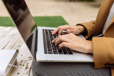 Hoher Winkel einer anonymen Studentin, die im Innenhof der Universität mit einem Laptop sitzt und Hausaufgaben macht, während sie in die Kamera schaut und lächelt - ADSF21681