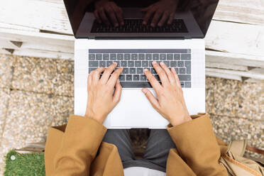 High angle of anonymous female student sitting in university courtyard with laptop and doing homework while looking at camera and smiling - ADSF21682