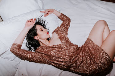 From above of alluring young female with long dark hair and makeup in fashionable mini dress with sequins sleeping on comfortable bed - ADSF21727