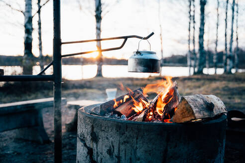 Gemütliches Lagerfeuer mit heller Flamme Heizung Metall Topf im Wald im Winter bei Sonnenuntergang - ADSF21752