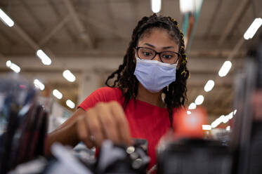 Afro latina young woman wearing a face mask selecting products in store - ADSF21788