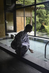 Junge kaukasische Frau in einem Kimono, die das Thermalwasser berührt, bevor sie ein traditionelles Bad in einem japanischen Onsen genießt - ADSF21791