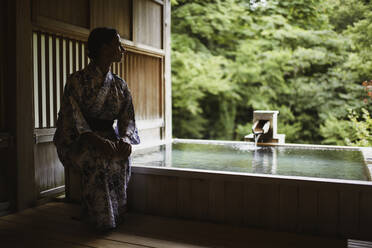 Junge kaukasische Frau im Kimono macht sich bereit, ein entspannendes und traditionelles Thermalwasserbad in einem japanischen Onsen zu genießen, Seitenansicht - ADSF21793