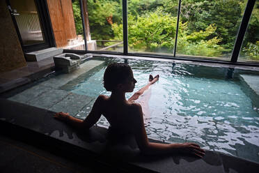 Silhouette einer jungen kaukasischen Frau, die ein entspannendes Thermalwasserbad in einem traditionellen japanischen Onsen-Ryokan genießt, Blick von hinten - ADSF21799