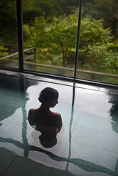 Silhouette of young caucasian woman enjoying.a relaxing thermal waters bath at a traditional Japanese onsen ryokan, view from behind - ADSF21804