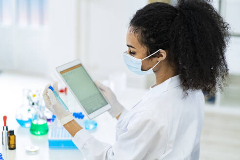 Forscher betrachtet Reagenzglas und digitales Tablet bei der Arbeit im Labor - GIOF11862