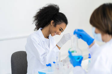 Smiling female researcher working with coworker while experimenting in laboratory - GIOF11880