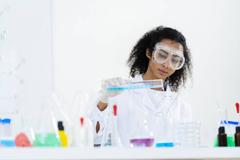 Junge Forscherin gießt Flüssigkeit in einen Kolben, während sie einen medizinischen Test im Labor durchführt - GIOF11904