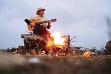 Mature man playing guitar against sky - JCMF01919