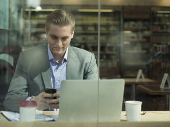 Handsome businessman using mobile phone in front of laptop at cafe - AJOF01271