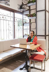 Smiling woman using laptop at table in cafe - LJF02122