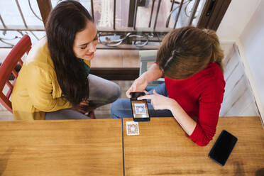 Frau scannt QR-Code mit ihrem Handy vor einer Freundin am Tisch in einer Bar - LJF02146