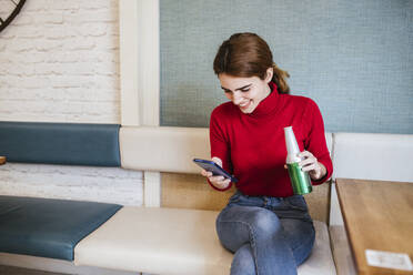 Glückliche Frau, die ein Smartphone benutzt, während sie in einer Bar Bier trinkt - LJF02149