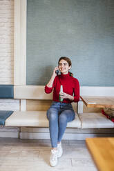 Lächelnde Frau, die eine Bierflasche hält, während sie in einer Bar mit ihrem Smartphone telefoniert - LJF02151