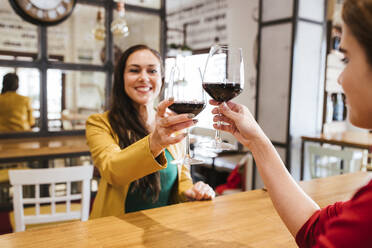 Glückliche Freundinnen stoßen mit Gläsern Wein am Tisch in einer Bar an - LJF02154