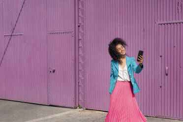 Smiling young woman taking selfie in front of purple metallic cabin - TCEF01673