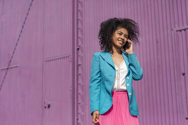 Smiling woman with Afro hairstyle talking on phone during sunny day - TCEF01674