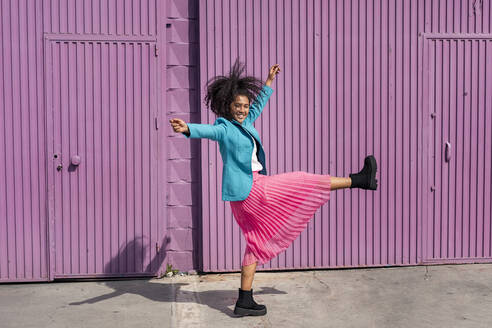 Carefree young woman dancing in front of purple cabin - TCEF01675