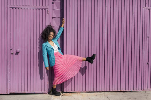 Smiling young woman while dancing by metallic purple wall - TCEF01677