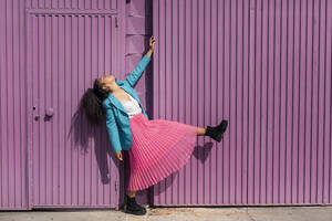 Junge Frau tanzt an einer lila Hütte an einem sonnigen Tag - TCEF01678