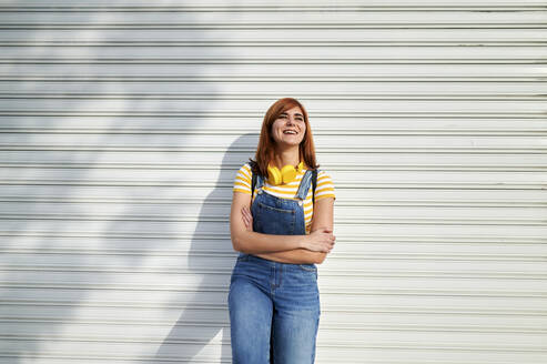 Smiling woman standing with arms crossed in front of metal shutter - KIJF03656
