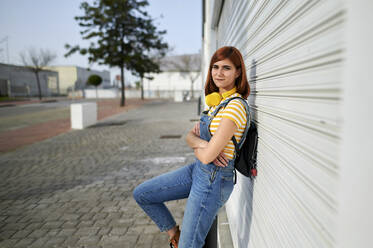 Junge Frau in Latzhose vor weißem Metallfensterladen stehend - KIJF03657