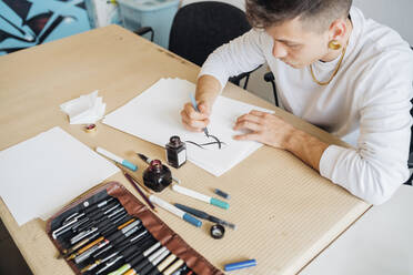 Hipster junger Mann übt Kalligraphie auf Papier im Atelier - MEUF02116