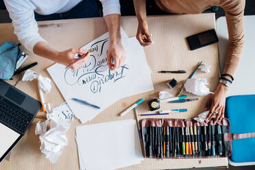 Young multi ethnic couple working together on calligraphy writing at studio - MEUF02133