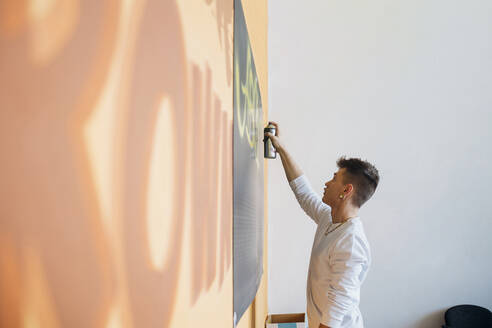 Hipster-Mann sprüht Farbe auf schwarzes Brett im Studio - MEUF02139