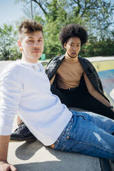 Young couple sitting at skateboard park during sunny day - MEUF02149