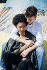 Freund umarmt Freundin beim Sitzen im Skateboardpark - MEUF02154