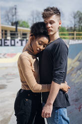 Afro woman hugging boyfriend while standing at skateboard park - MEUF02159