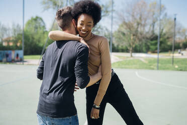 Smiling Afro woman hugging boyfriend at sports court - MEUF02162