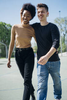 Cheerful couple walking at sports court during sunny day - MEUF02169