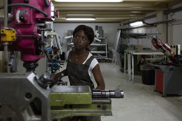 Professionelle junge afroamerikanische Mechanikerin bei der Bearbeitung von Details an einer Drehmaschine in einer Reparaturwerkstatt - ADSF21875