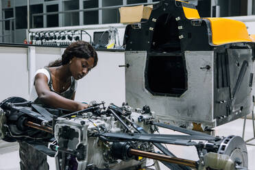 Seriöser junger afroamerikanischer Mechaniker, der ein Fahrzeug in einem modernen Reparaturzentrum zusammenbaut - ADSF21878