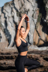 Flexible Frau in Sportkleidung balanciert auf einem Bein in Vrksasana mit erhobenen Armen beim Yoga in den Bergen im Sommer - ADSF21889