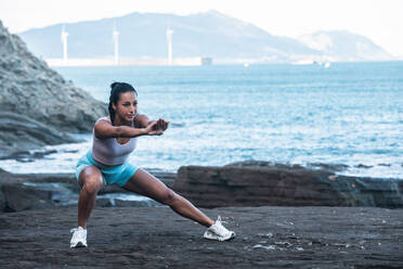 Friedliche Frau in Sportkleidung macht Yoga und balanciert in Skandasana, während sie in der Natur Achtsamkeit übt und in die Kamera schaut - ADSF21890