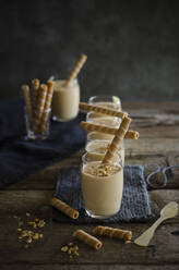 Hoher Blickwinkel auf appetitliches Nougatmousse-Dessert in Gläsern, dekoriert mit gestreiften Waffelröllchen und Nüssen, serviert auf einem Holztisch in der Küche - ADSF21899