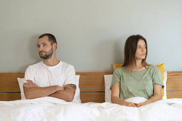 Frustrated young couple sitting on bed while looking away from each other at home - SBOF03184