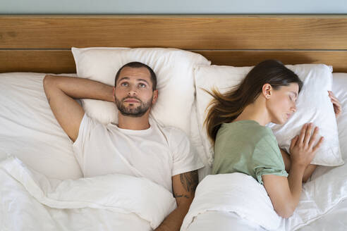 Junge Frau schläft neben einem besorgten Mann, der an die Decke starrt, während er zu Hause auf dem Bett liegt - SBOF03186