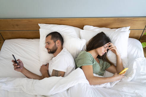 Junges Paar benutzt Smartphones, während es Rücken an Rücken zu Hause im Bett liegt - SBOF03187