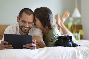 Frau umarmt Freund Blick auf digitale Tablet, während auf dem Bett im Schlafzimmer zu Hause liegen - SBOF03192